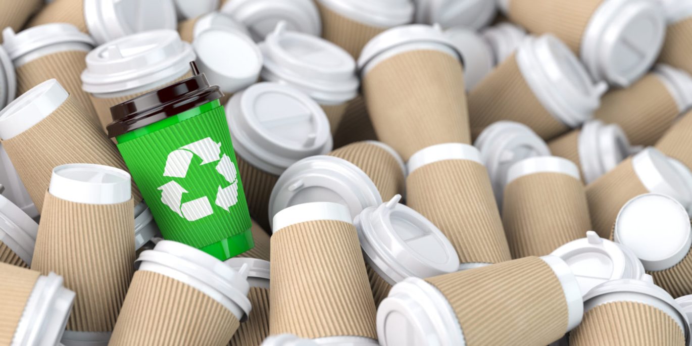 Recycling sign on one of the heap of many empty paper coffee cu